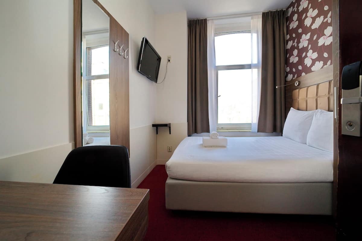 Une chambre d’hôtel avec un lit, un bureau, un téléviseur fixé au mur et une fenêtre avec des rideaux.