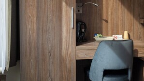 Hotelkamer met een houten garderobe, een bureau met stoel, een flatscreen televisie boven het bureau en een bed met wit beddengoed.