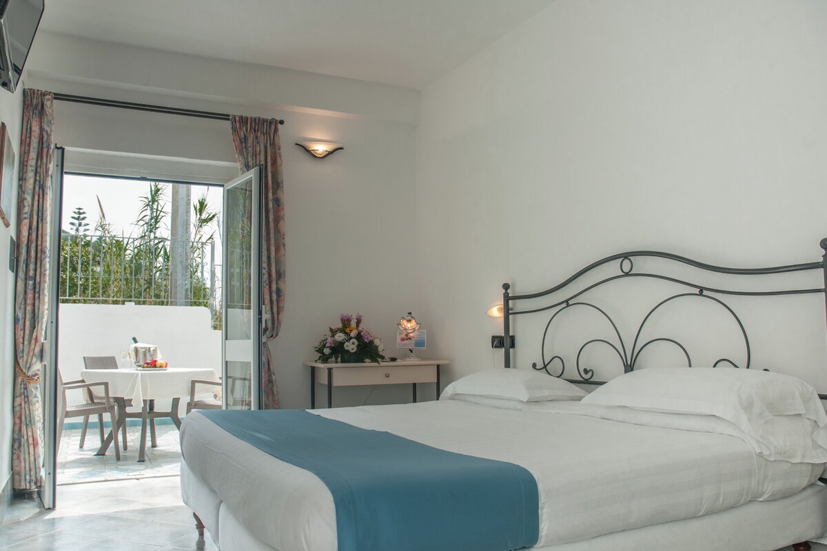 A bedroom with a bed, a desk with a lamp, and a view of the outdoors.