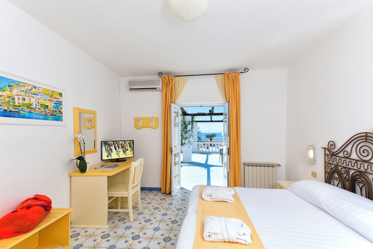 Ett hotellrum med en säng, ett skrivbord med en dator, en stol, ett fönster med gardiner och utsikt över omgivningen.