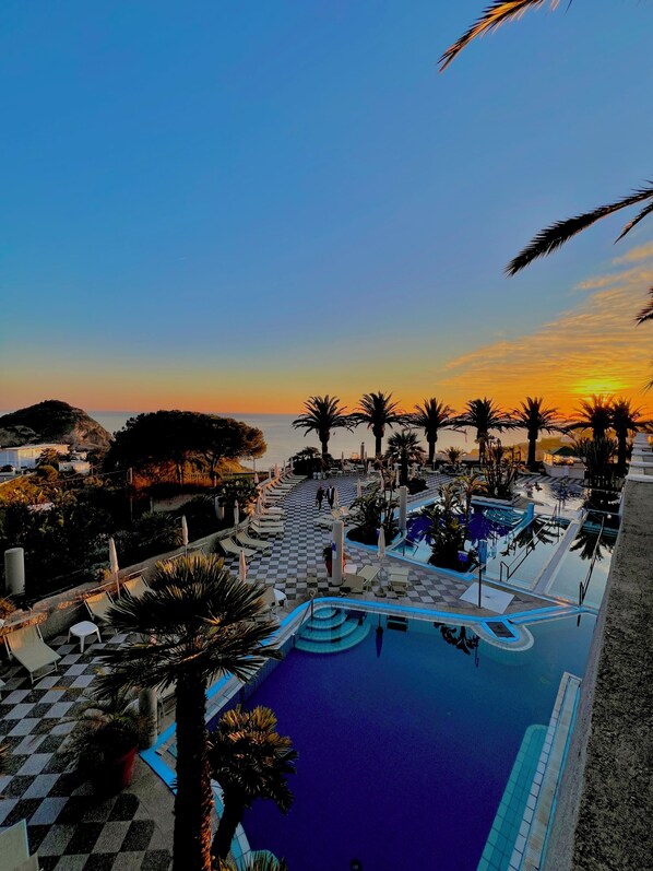 Zona de piscina de un resort con piso a cuadros, palmeras y vista al atardecer.