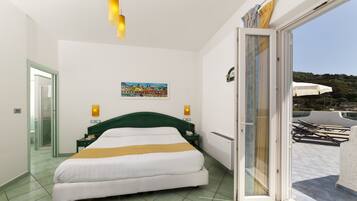 Habitación de hotel con cama, un cuadro, mesita de noche, teléfono y puerta corrediza de vidrio que da a un área exterior con sombrillas.