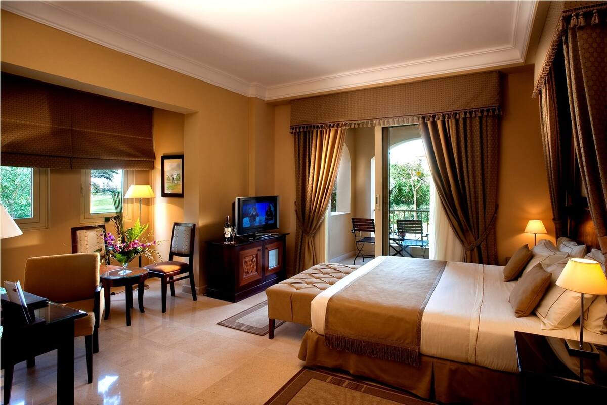 Une chambre d’hôtel avec un lit, un bureau, une chaise, une télévision et une fenêtre avec des rideaux.