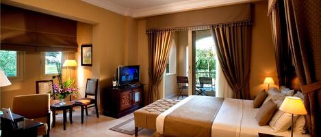 Una habitación de hotel con cama, escritorio, silla, televisor y ventana con cortinas.