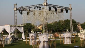 An outdoor wedding setup with a stage, tables, and chairs arranged on a lawn.