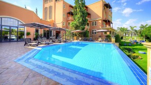 Piscina con sillas de descanso y sombrillas, rodeada por un edificio con varios balcones y cielo despejado.