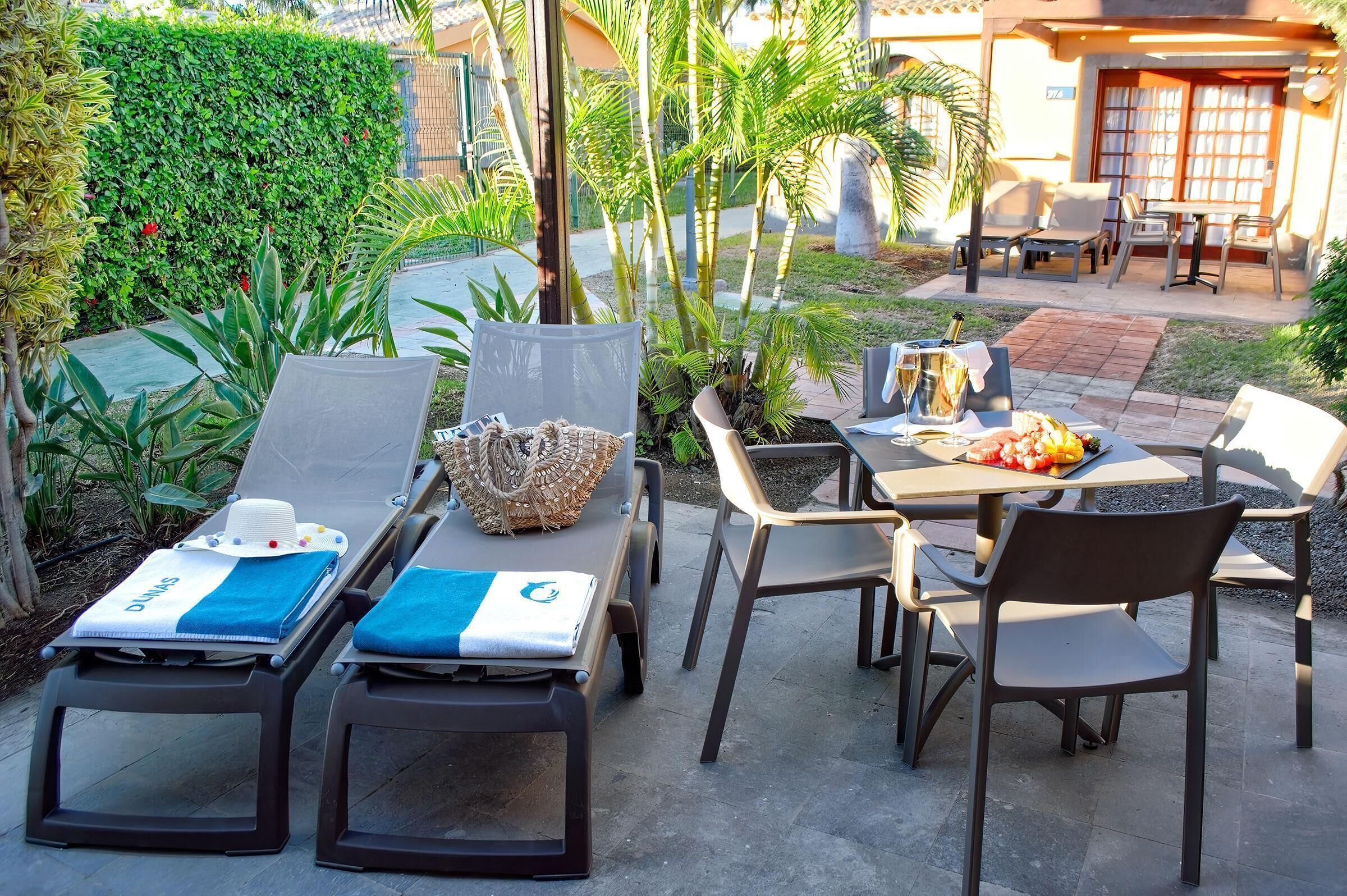 Eine Terrasse mit Liegestühlen, einem Tisch und Stühlen sowie ein kleiner Garten mit Pflanzen und einer Hecke.