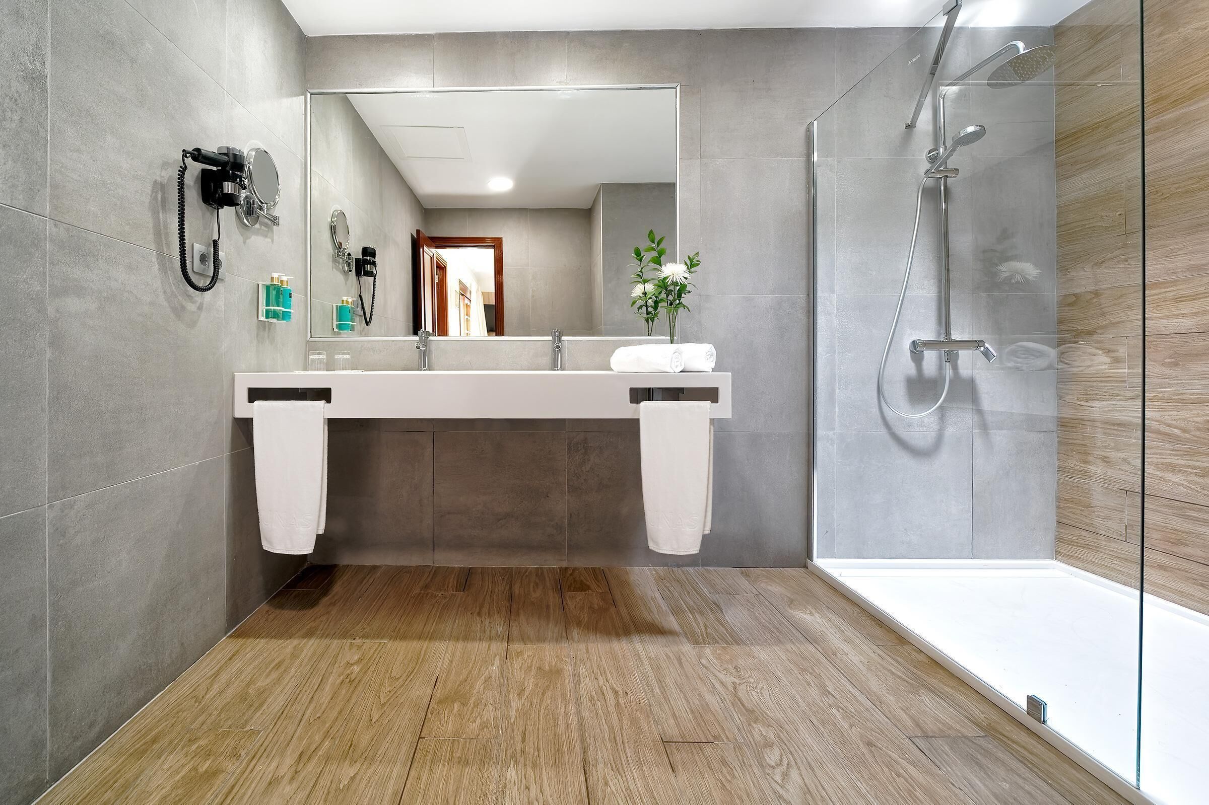 Une salle de bain moderne avec un grand miroir, deux vasques, une douche et un plancher en bois.