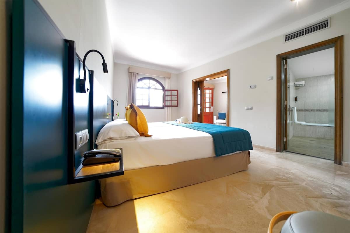 A bedroom with a bed, bedside table, lamp, and a view of the bathroom through an open door.