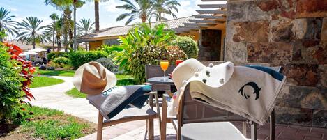 A patio area with two wicker chairs, a table, and a drink.