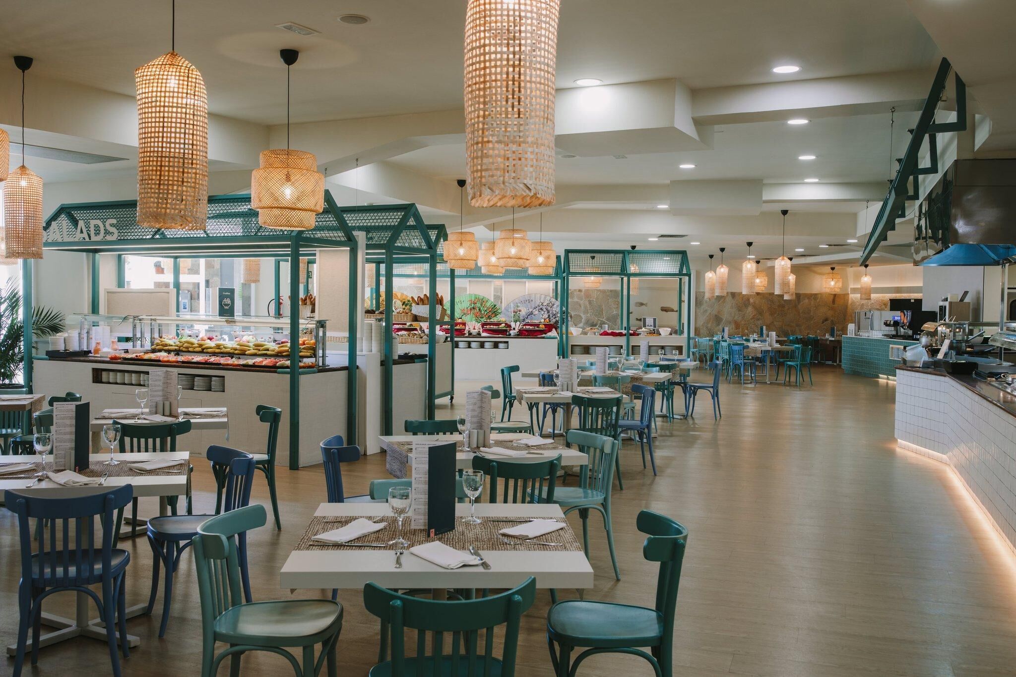 Un restaurante espacioso con techos altos, lámparas de mimbre colgantes y una zona central de servicio.