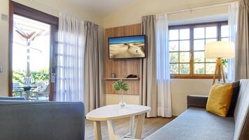 Habitación de hotel con sofá, una mesita con un jarrón, televisión en la pared y ventana con cortinas.