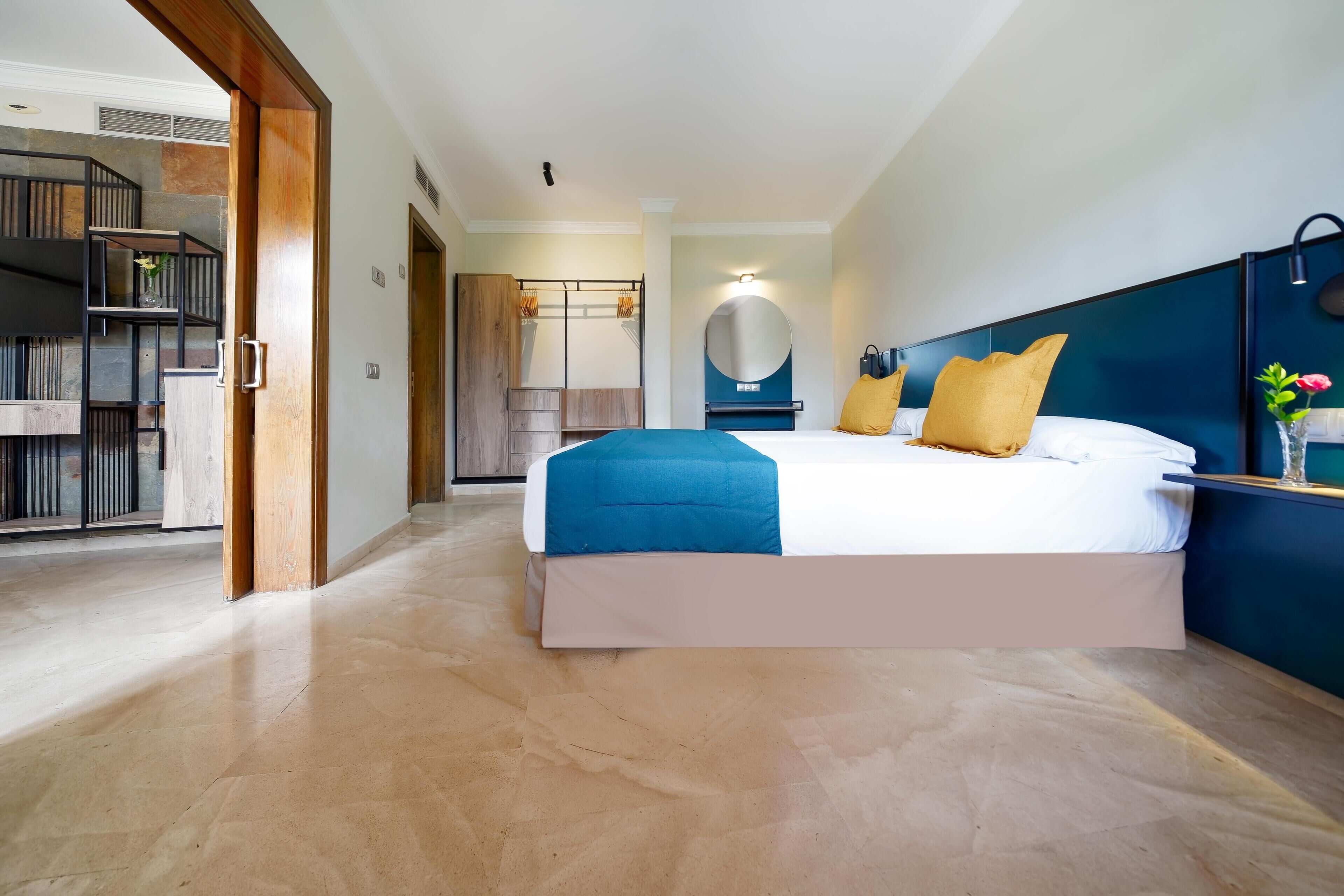 A modern hotel room with a large bed, a wooden wardrobe, a mirror, and a blue accent wall.