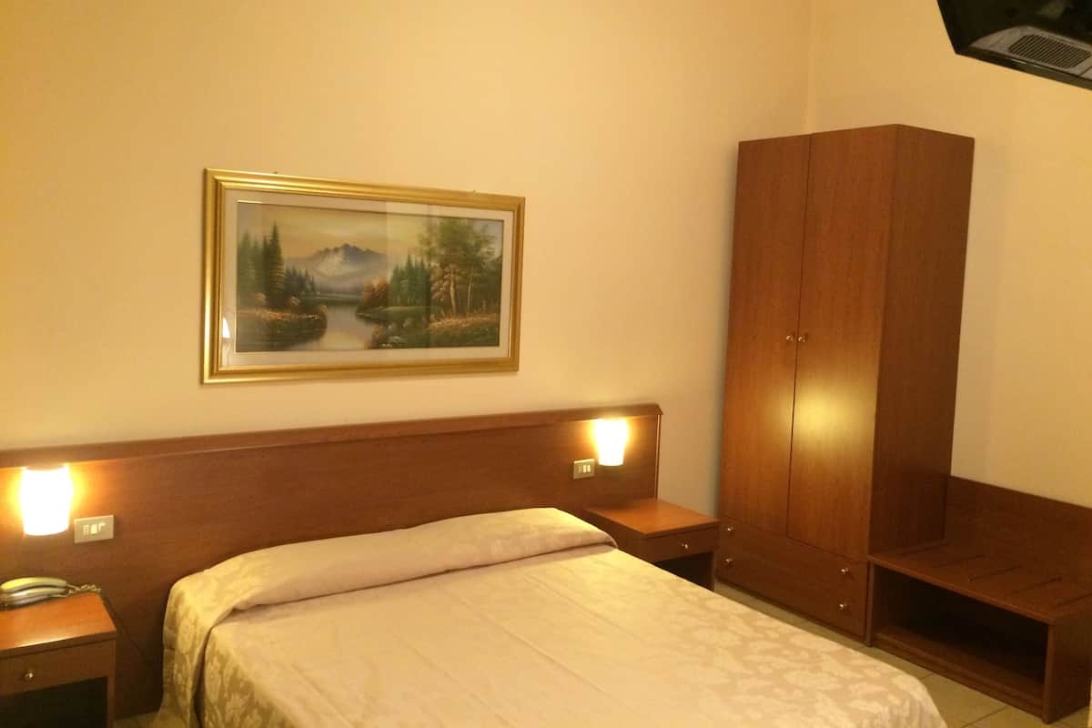 A hotel room with a bed, bedside lamps, a wardrobe, and a painting on the wall.