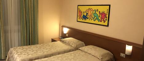 A hotel room with two beds, a nightstand with a phone, a wall-mounted light, and a colorful artwork.