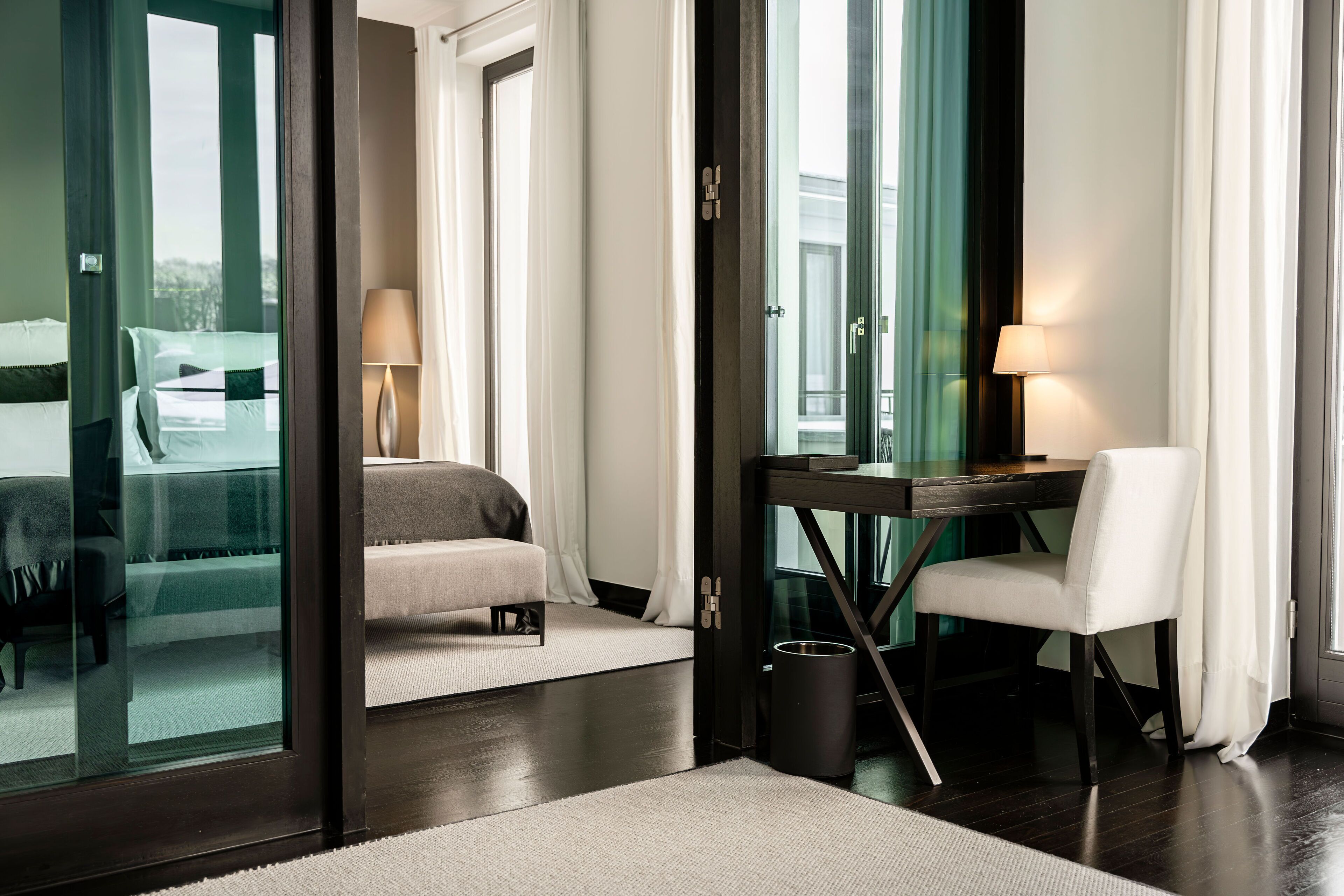 Habitación de hotel con cama, escritorio, silla, lámpara y vista a través de un ventanal.