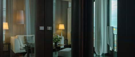 A hotel room with a sofa, armchair, and a small table with a lamp.