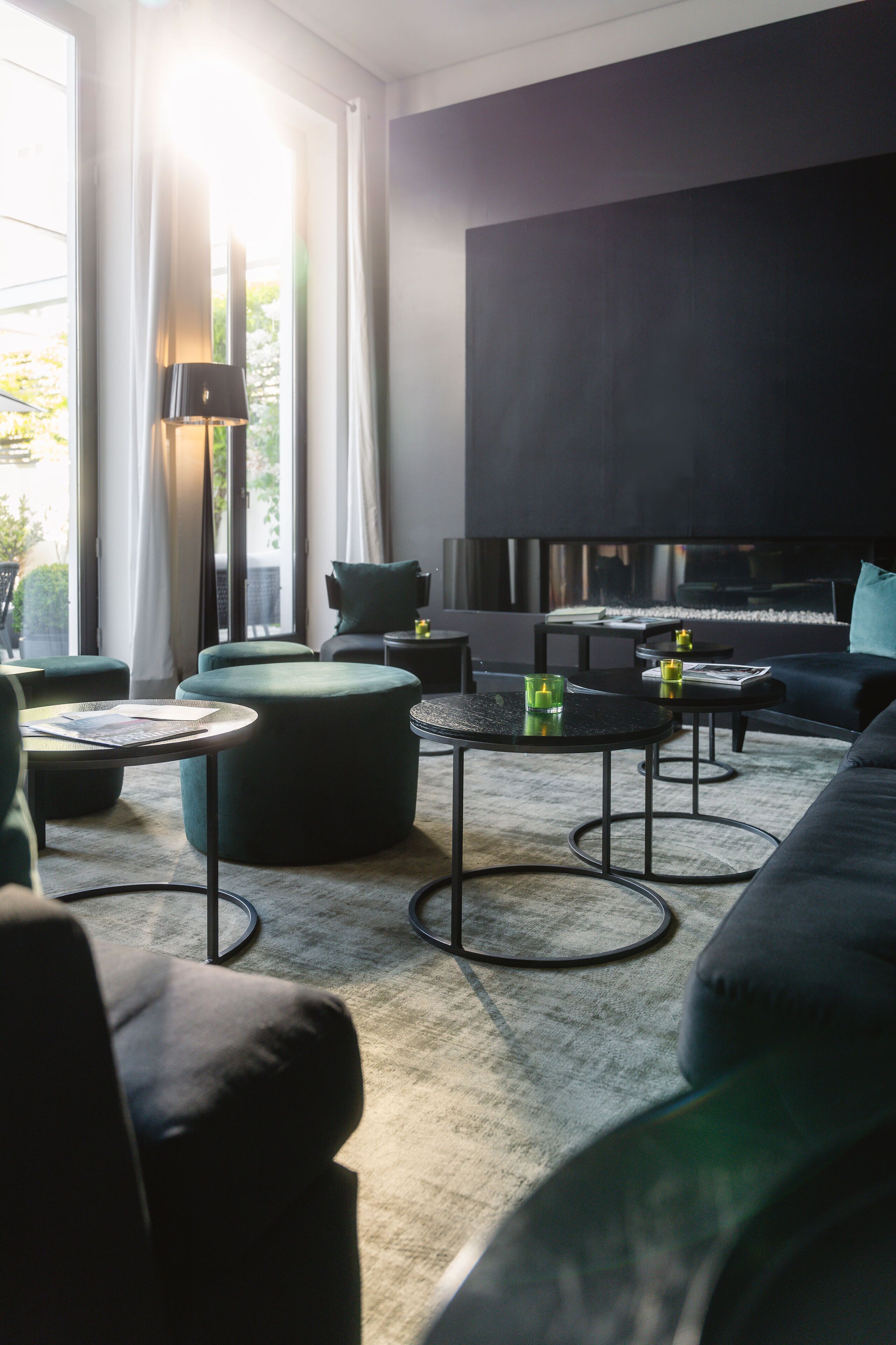 Ein modernes Wohnzimmer mit Sofa, Hocker und Couchtisch, einem Kamin und einem großen Fenster mit Vorhängen.