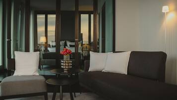A modern hotel room with a dark-colored sofa, a small round table, and a chair. There is a vase with red flowers on the table.
