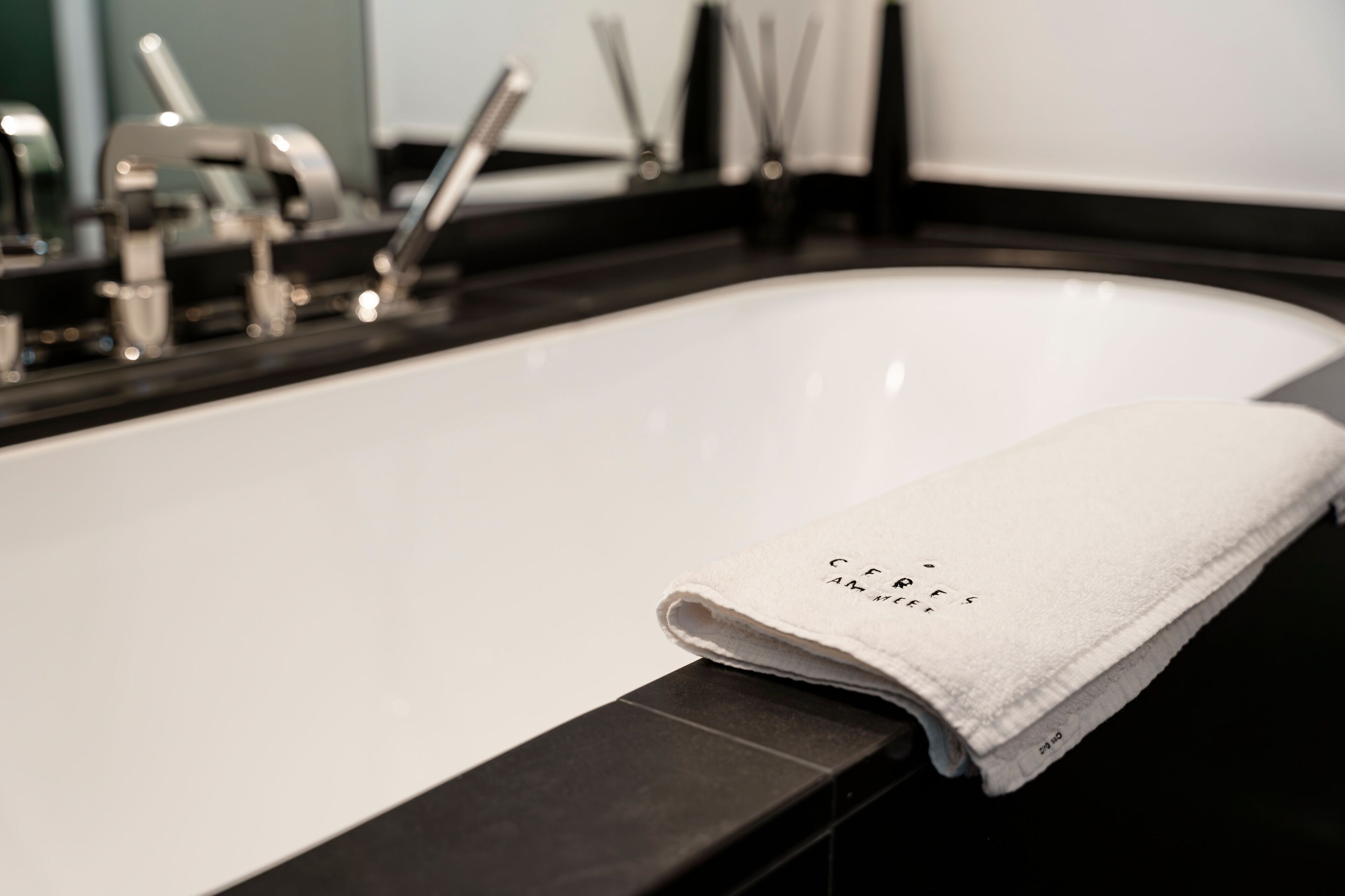 Une baignoire blanche avec une serviette posée sur le bord, un plan de travail noir et un miroir au-dessus du lavabo.
