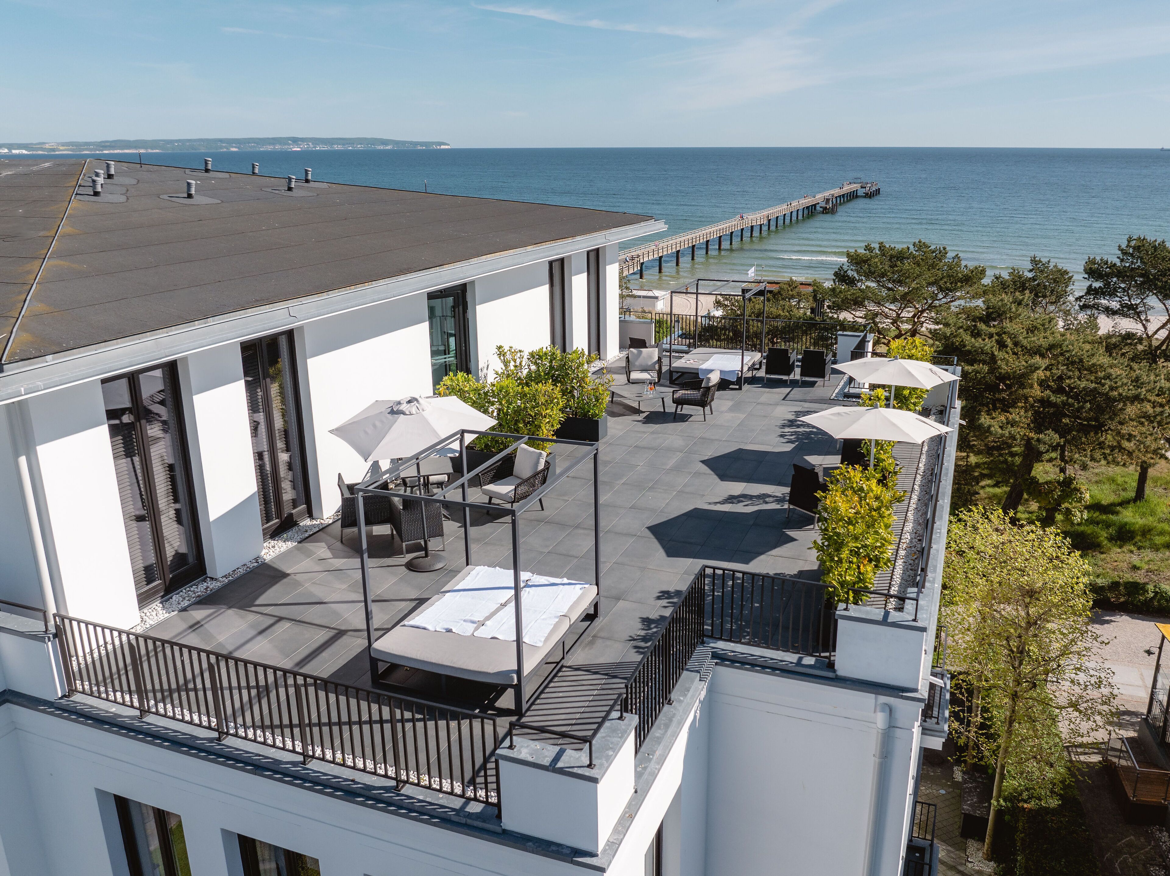A rooftop patio with outdoor seating, a view of the sea, and a pier in the distance.