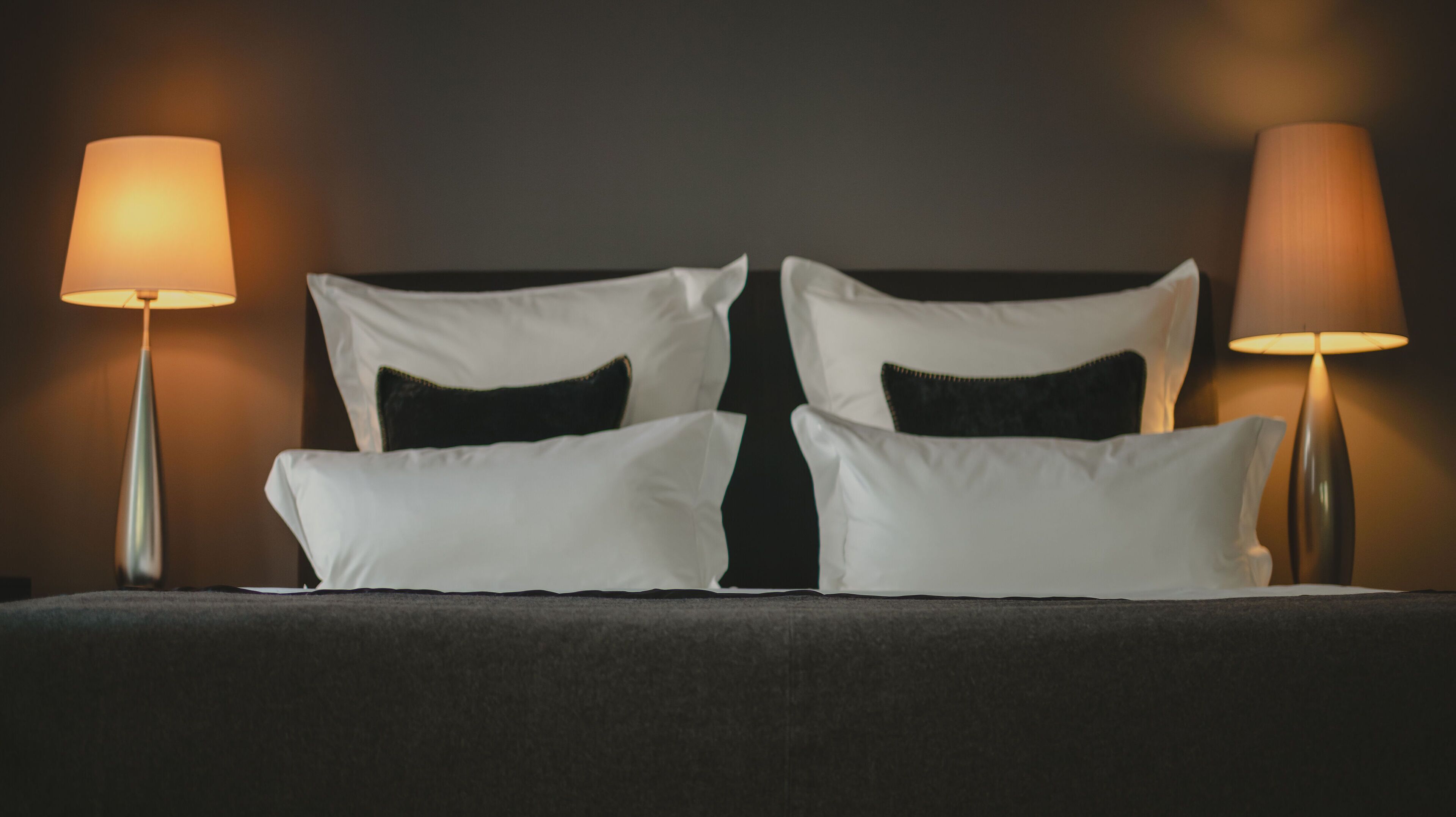 Un letto rifatto con cuscini bianchi e neri, illuminato da due lampade ai lati.