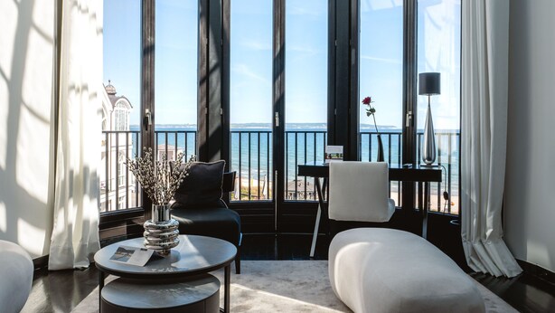 Un interior moderno con techo de vidrio, ventanas amplias, una mesa redonda, un sofá y vista al mar.