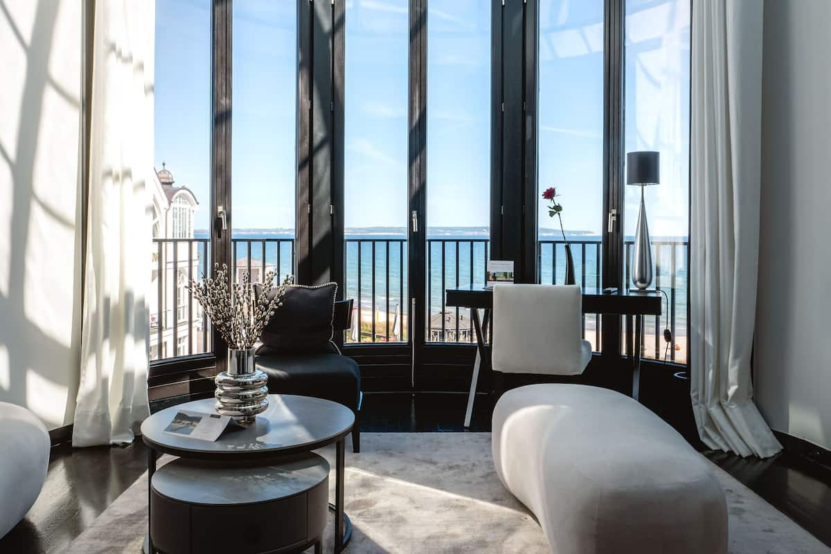 A modern interior with a glass ceiling, large windows, a round table, a sofa, and a view of the sea.