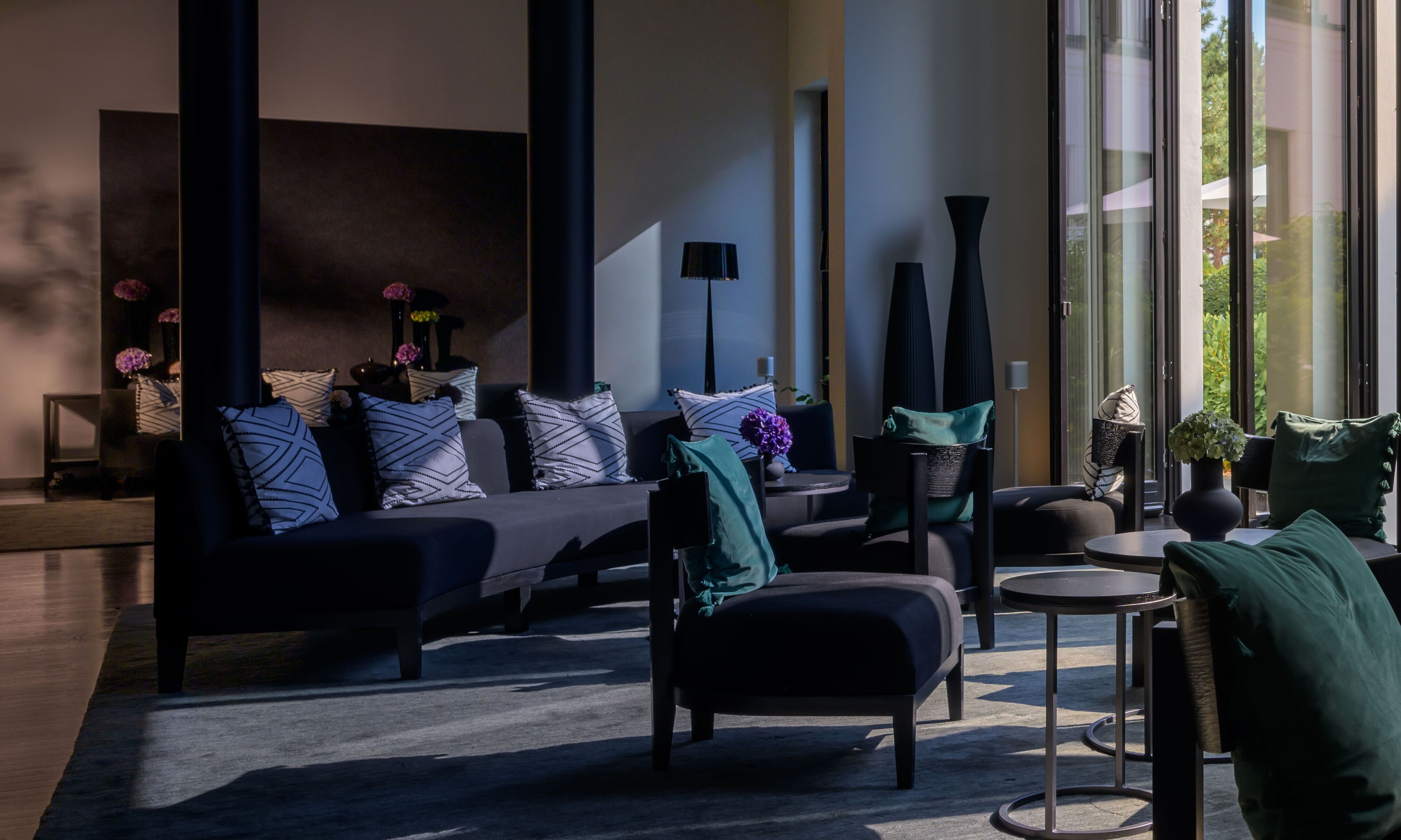 A modern living room with a sofa, chairs, and a coffee table. There is a large window providing natural light.