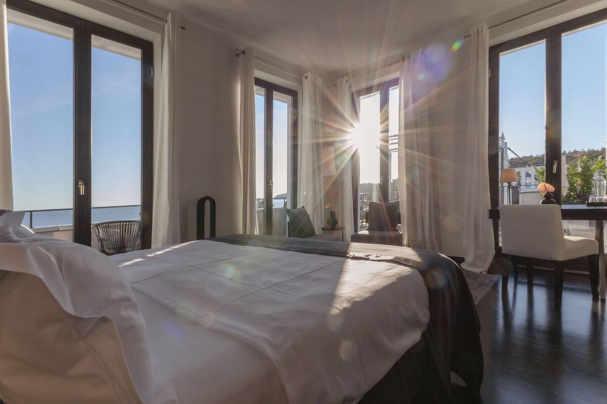 A hotel room with a large bed, a desk, and a view of the sea.