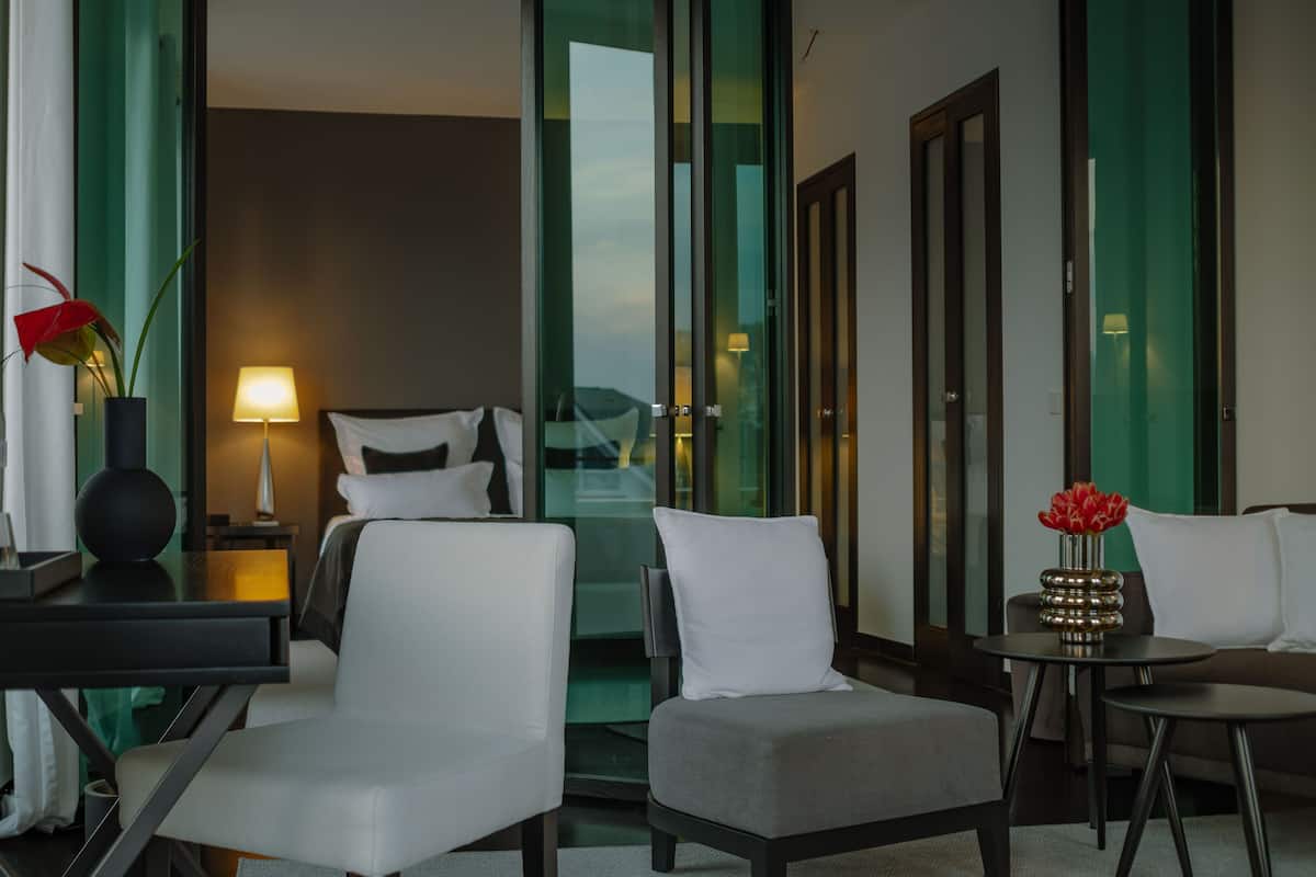 A hotel room with a bed, two chairs, a small table, a lamp, and a vase with flowers.