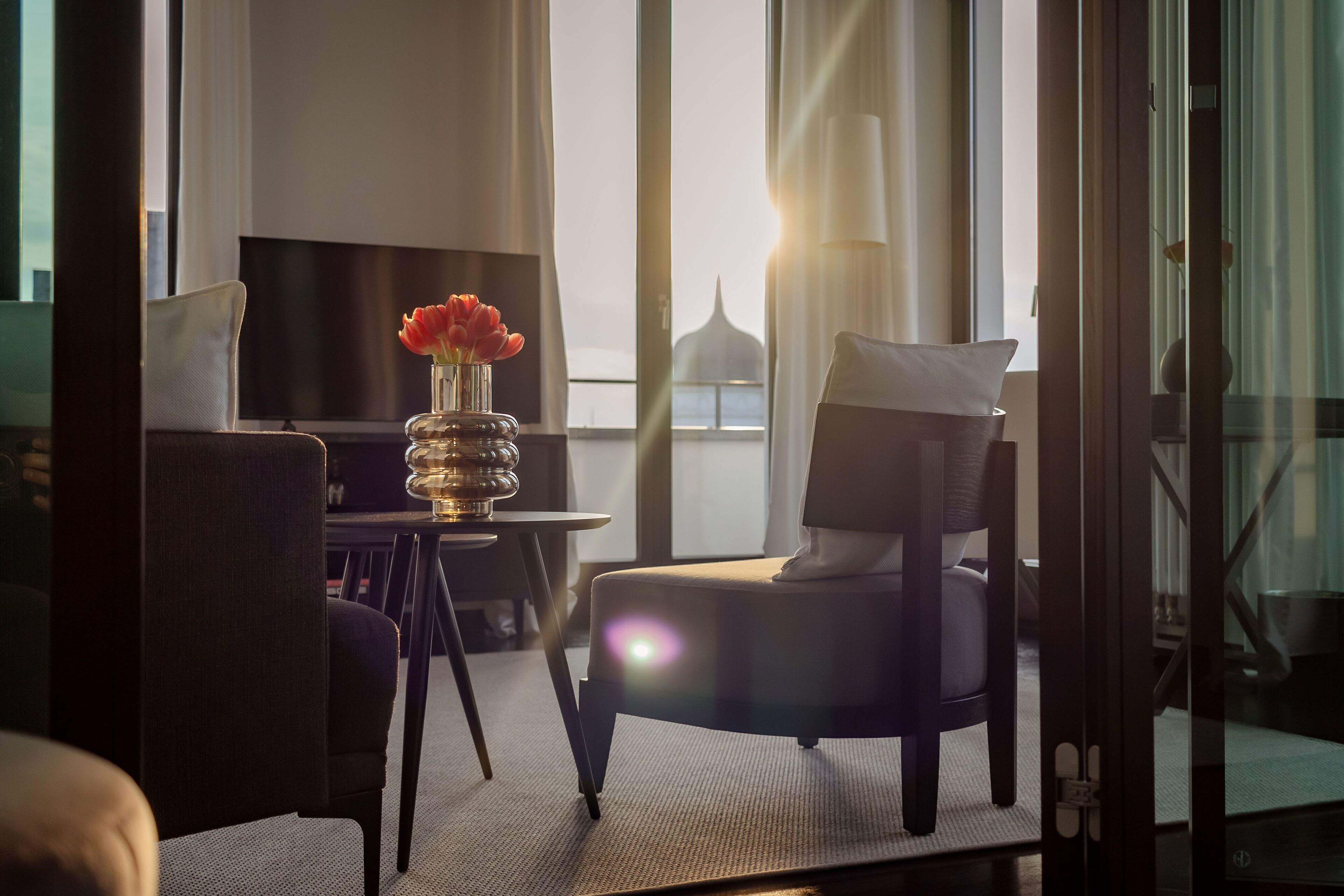Ein modernes Hotelzimmer mit einer Couch, einem kleinen Tisch mit Blumenvase und einem Fernseher.