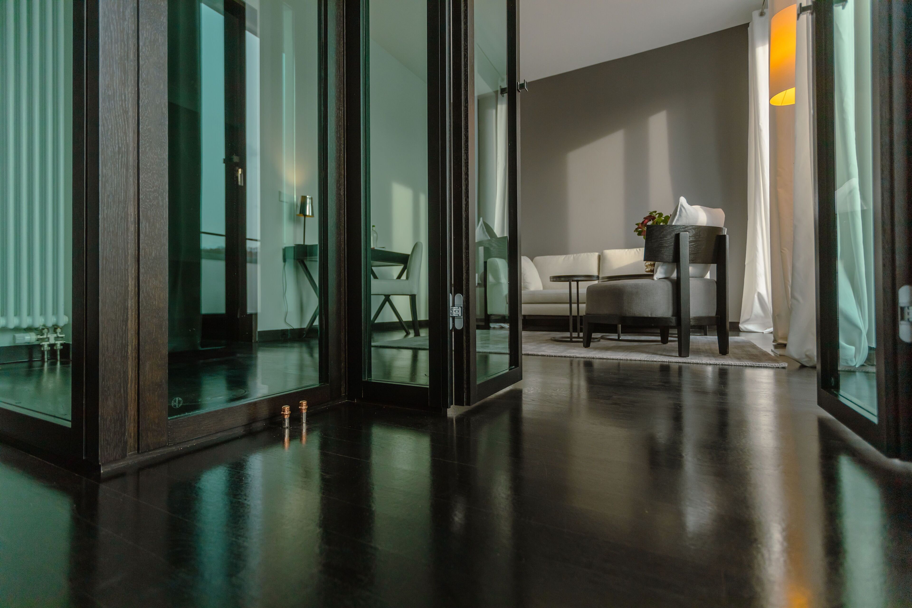 A modern hotel lobby with a glass partition, a sofa, a small table, and a potted plant.