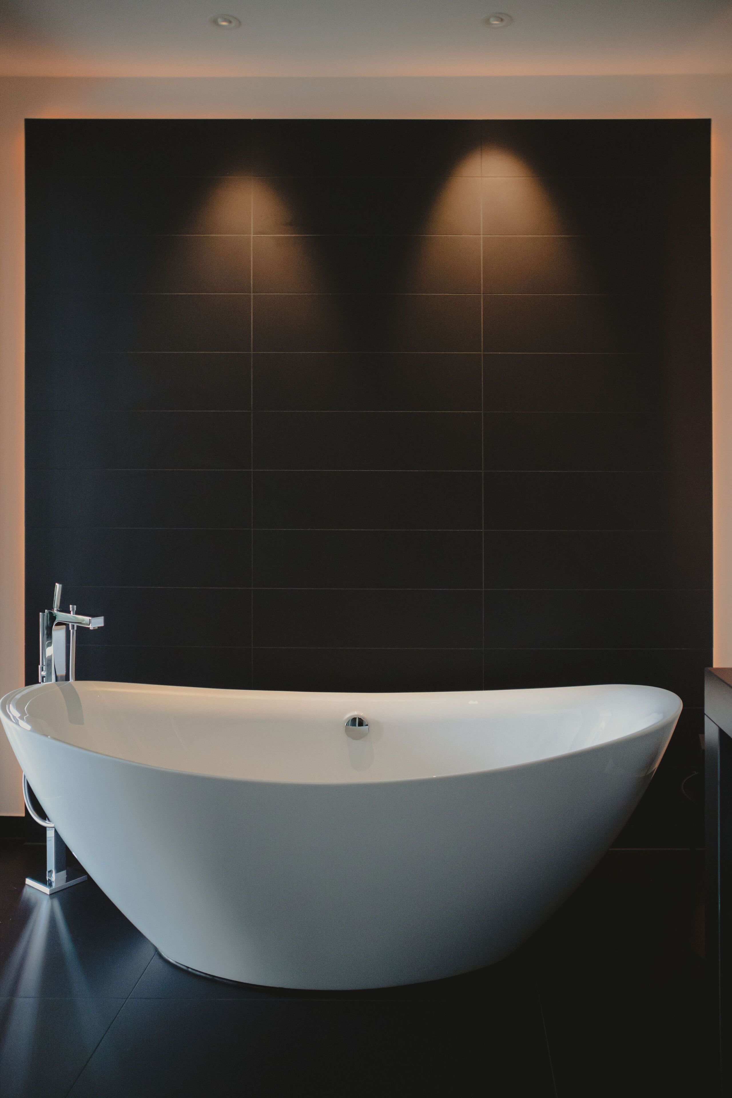 Un baño moderno con una bañera independiente, paredes de azulejos oscuros y un diseño minimalista.