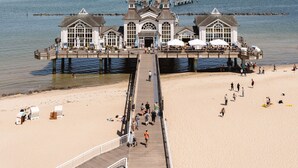 Un muelle que se adentra en el mar, con un edificio al final, una playa de arena y un cielo despejado.