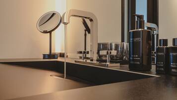 A modern bathroom with a sleek black sink, a large mirror, and a built-in faucet. There are several bottles of Noir body lotion and shampoo on the counter.