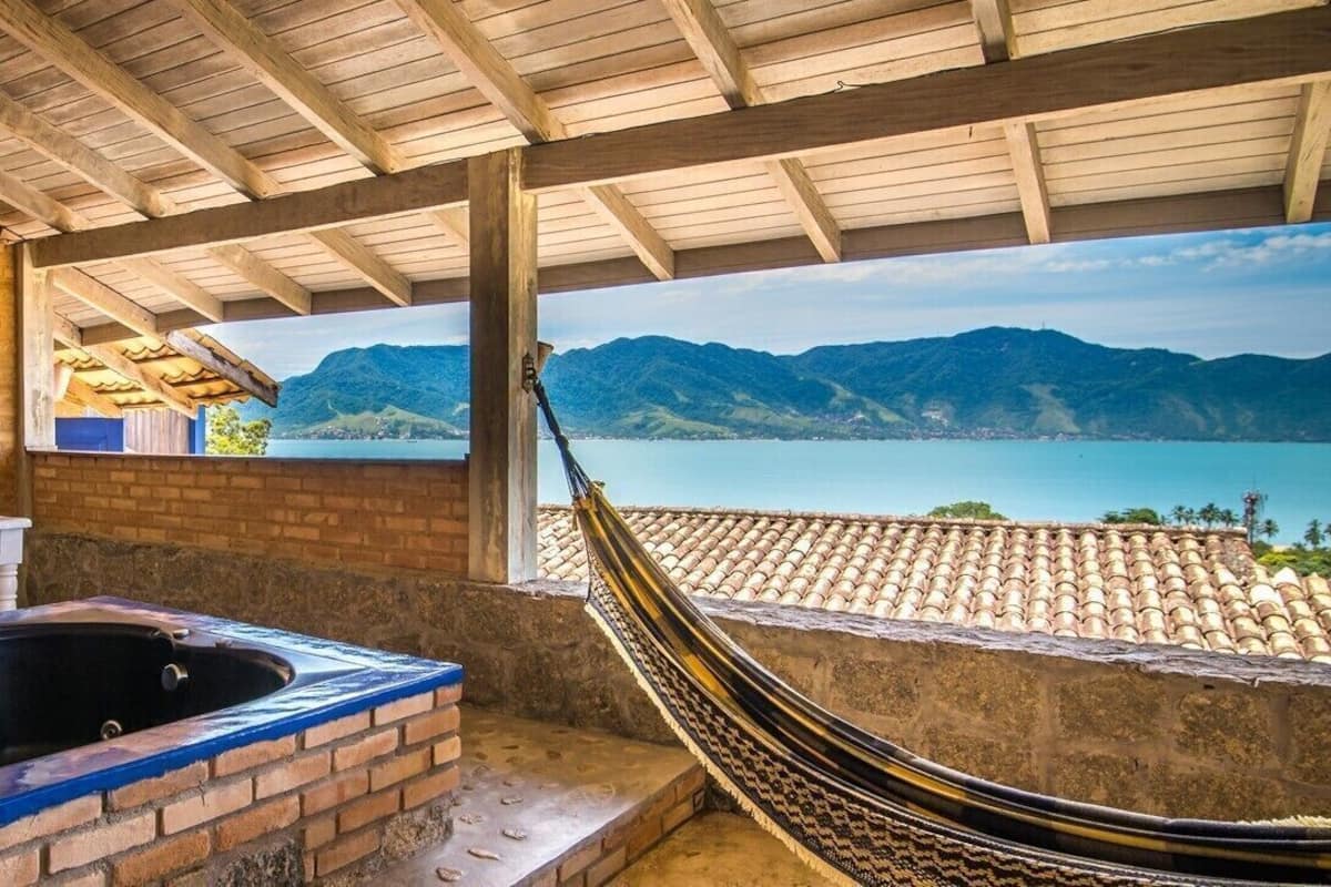 A hammock under a wooden roof, a brick wall, and a view of mountains and water.