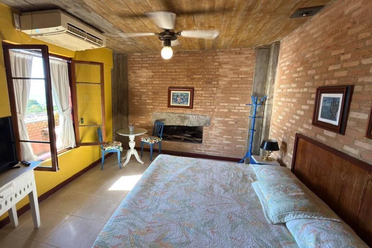 A room with a brick fireplace, a bed with patterned bedding, a ceiling fan, and a television on a stand.