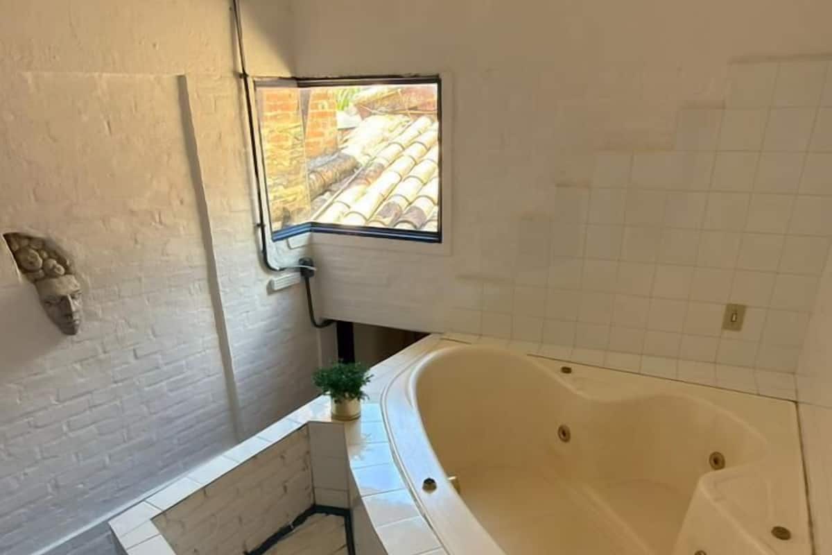 A bathroom with a large bathtub, a small window, and a wooden staircase.
