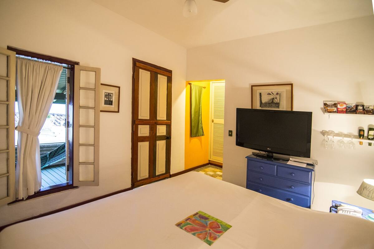 A hotel room with a bed, a television, a blue dresser, a door, and a window with curtains.