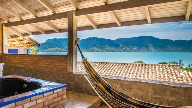A hammock under a wooden roof with a view of mountains and a lake. -  Maison Joly Residence (Ilhabela)