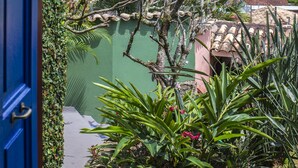 A view from a balcony overlooking a body of water, with mountains in the distance and a building with a red roof. -  Maison Joly Residence (Ilhabela)