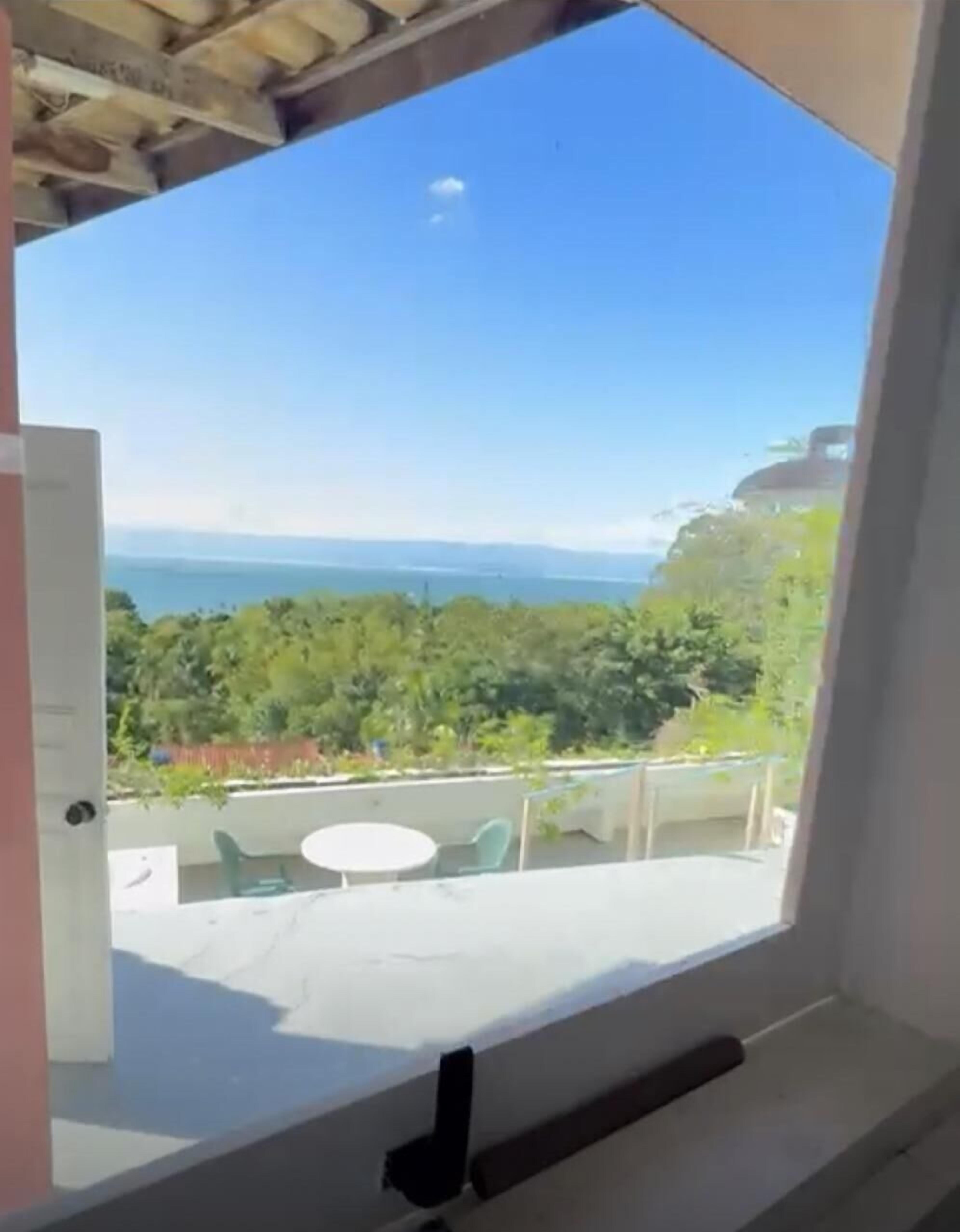 Un balcón con vista a un paisaje costero, incluyendo árboles y una masa de agua distante.