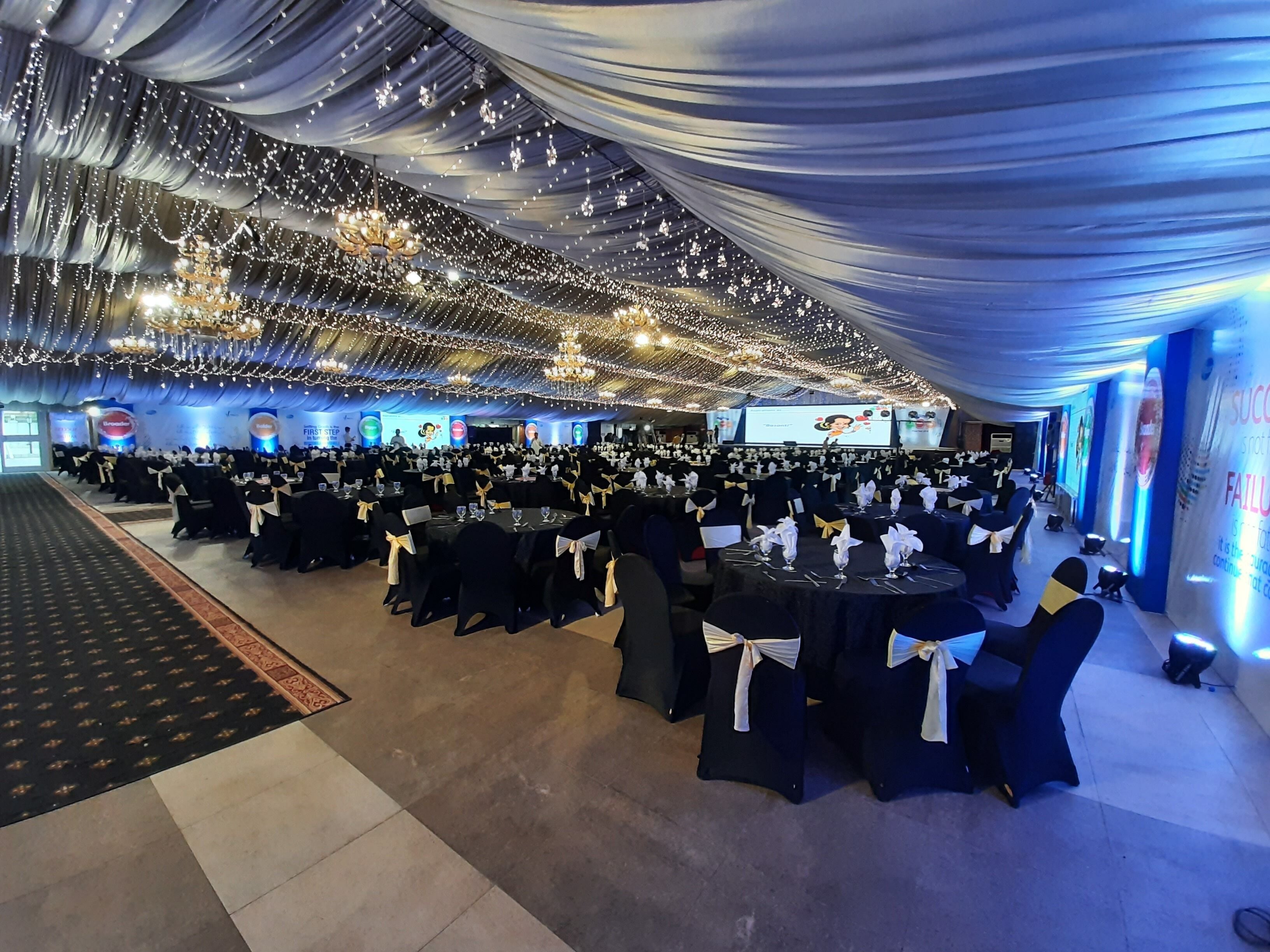 A banquet hall with rows of tables, chairs, and a stage with a screen.