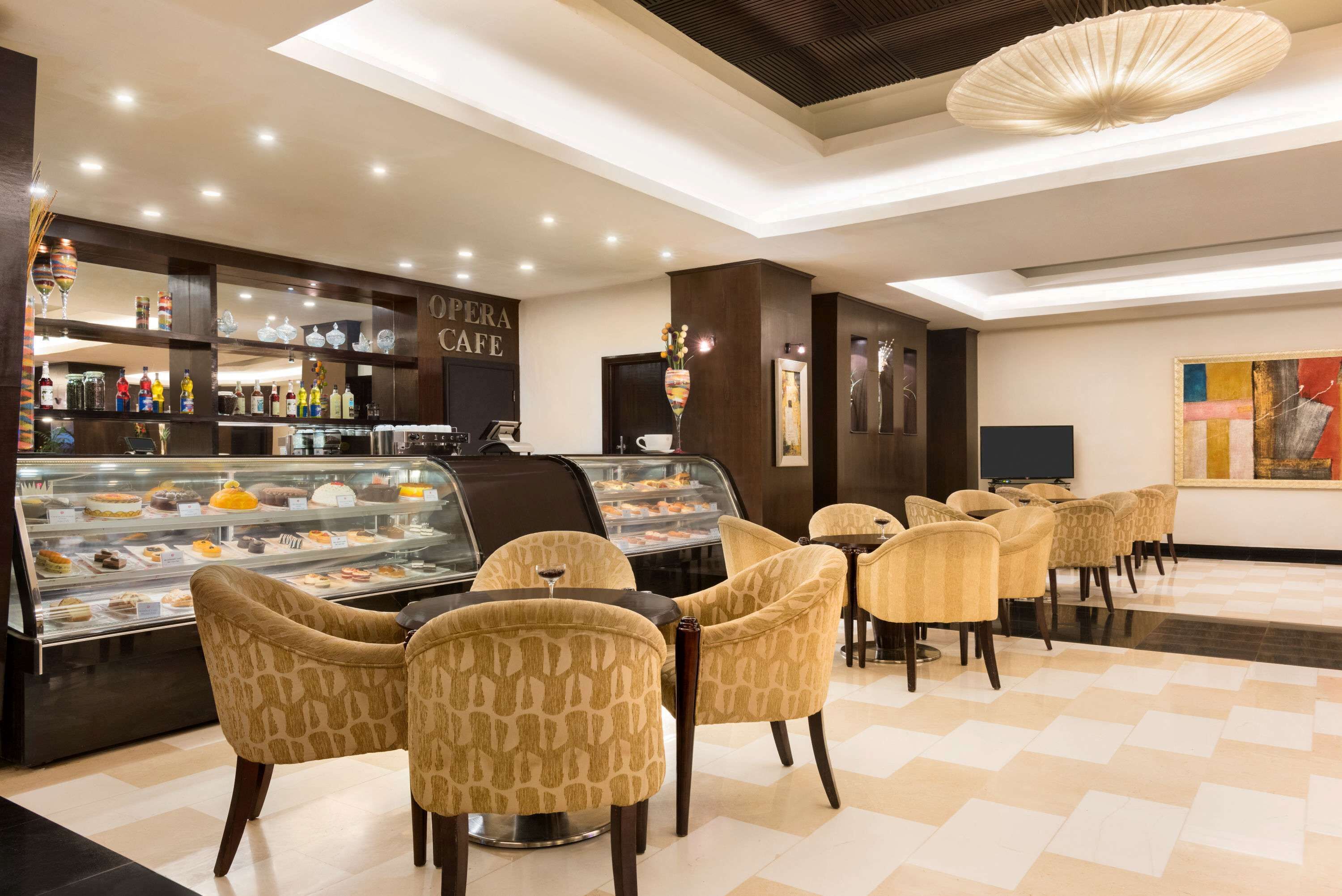Un café moderno con una vitrina de pasteles, sillas estampadas y una zona de bar con botellas de licor.