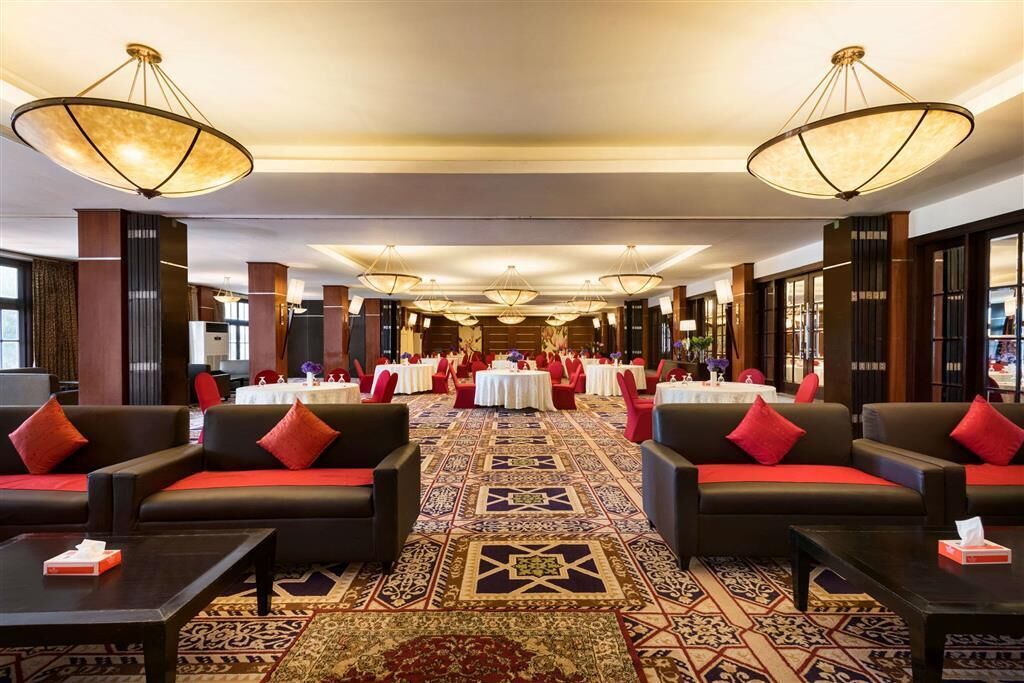 A spacious hotel lobby with multiple seating areas, tables set for dining, and large chandeliers.