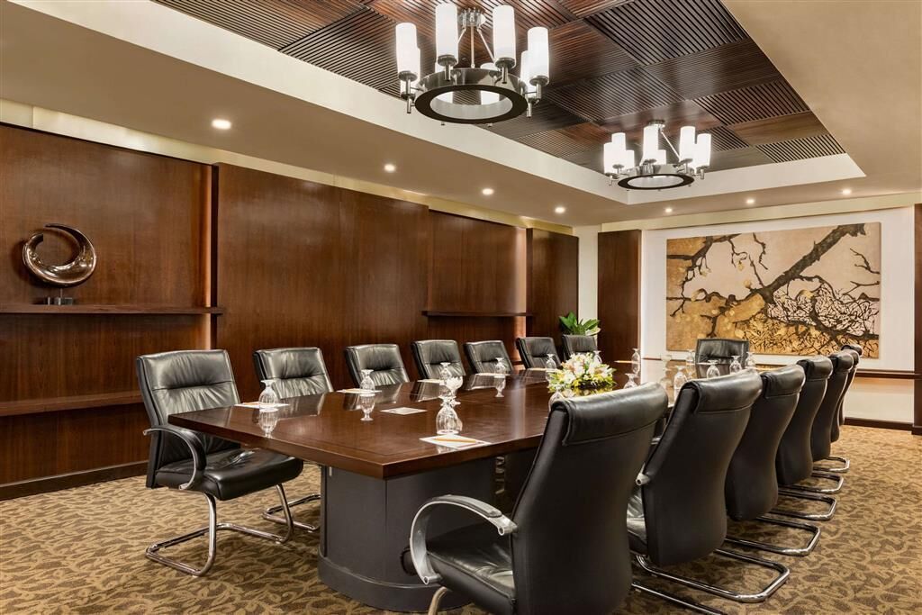 Une salle de conférence dotée d’une grande table, de fauteuils en cuir noir et d’un lustre.
