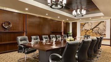 A conference room with a large table, black leather chairs, and a chandelier.