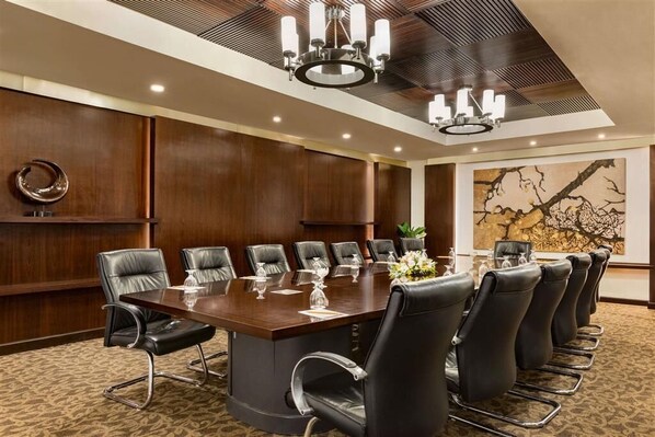 A conference room with a large table, black leather chairs, and a chandelier.