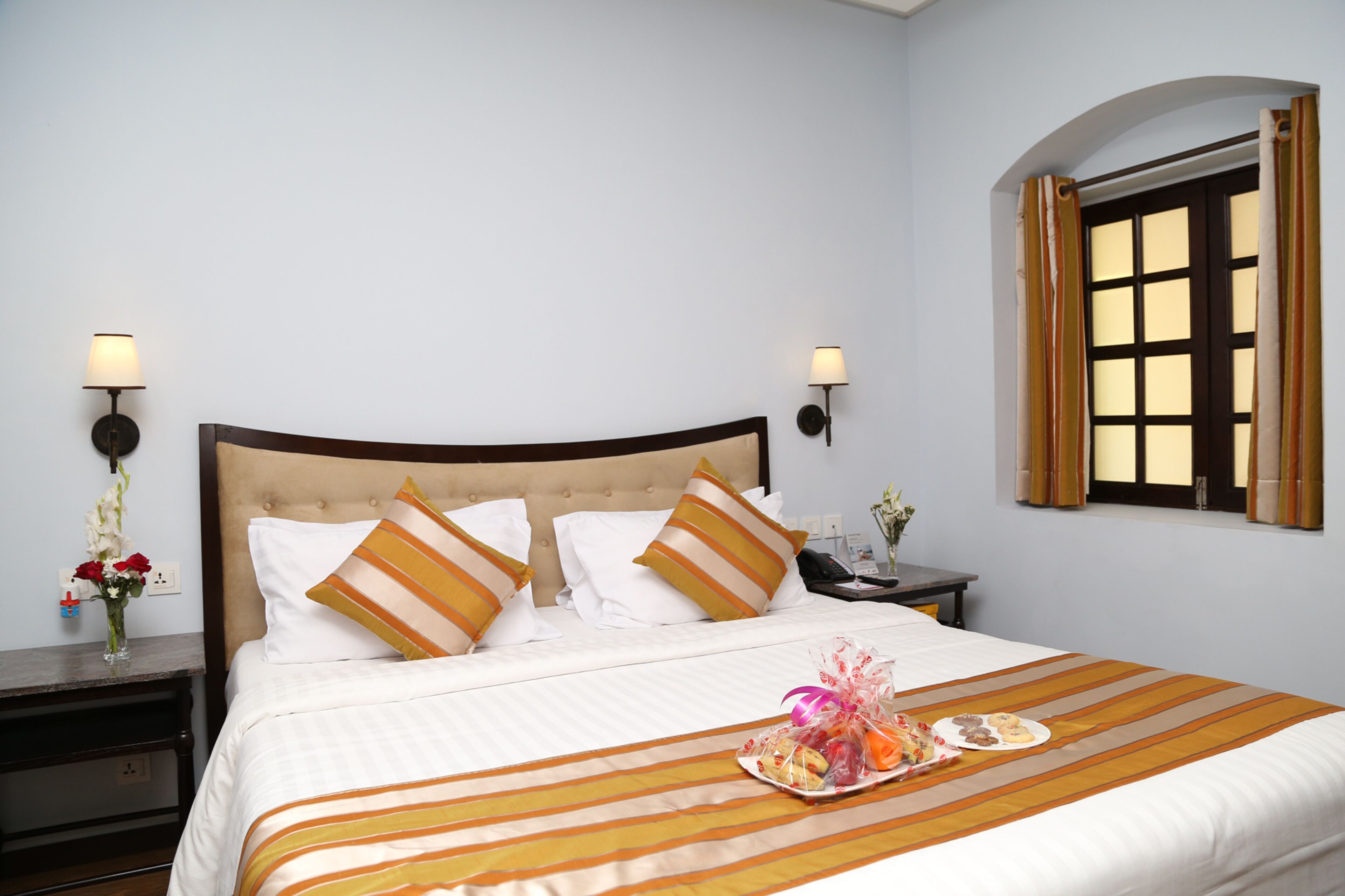 Habitación de hotel con cama, dos lámparas de noche, mesita de noche, bandeja de comida y ventana con cortinas.